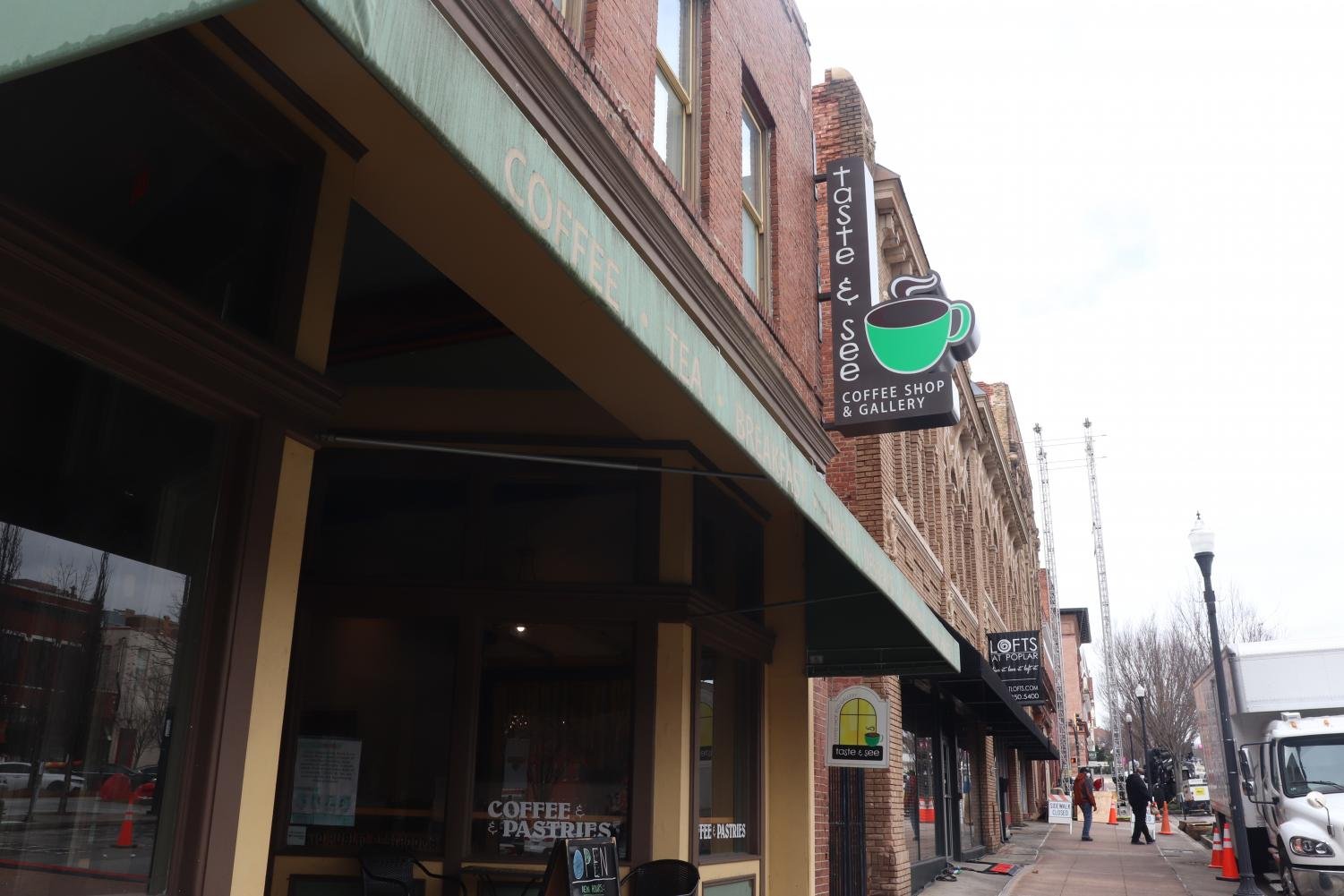 Taste+and+See Exterior view of Taste & See coffee shop and gallery, featuring a green awning and a sign displaying coffee offerings. The image captures the historic brick buildings lining the street, with pedestrians and vehicles visible in the background. Ideal for showcasing local coffee culture and inviting atmosphere.
